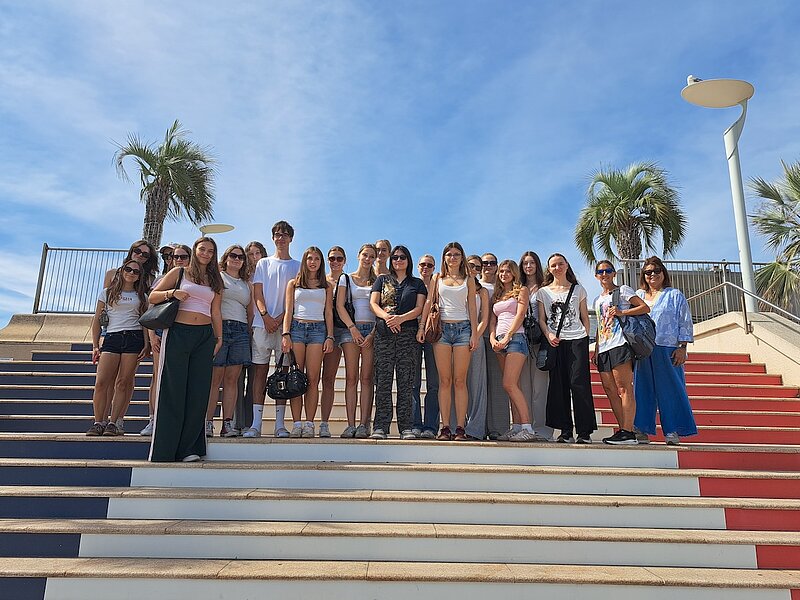 Jugendgruppe steht auf bunten Stufen vor Palmen am Meer