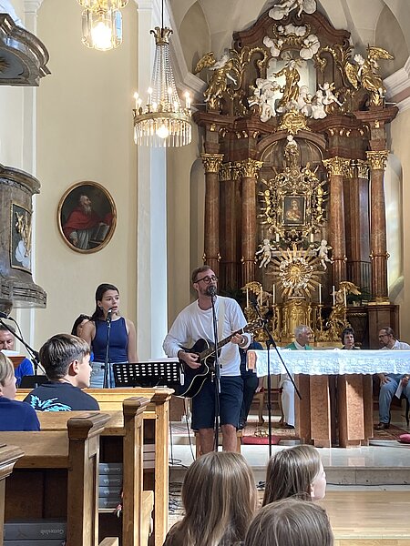 Gitarrist und Sängerin treten in einer Kirche mit barockem Altar auf.