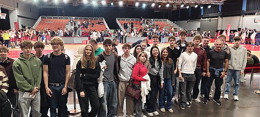 Jugendliche in Sporthalle mit Zuschauertribüne im Hintergrund